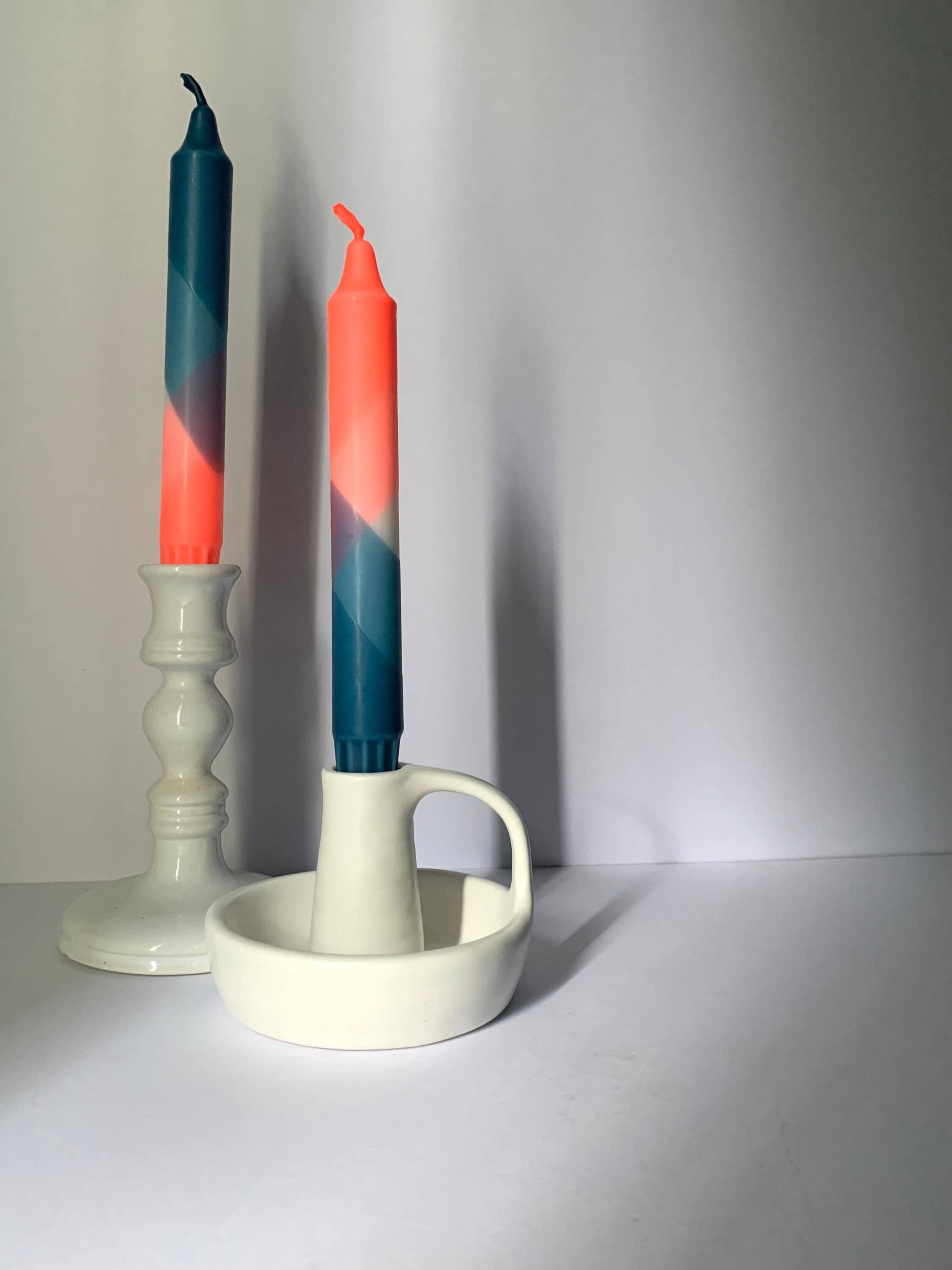 Two colorful candles in a white candle holder on a plain background by The Singing Rabbit