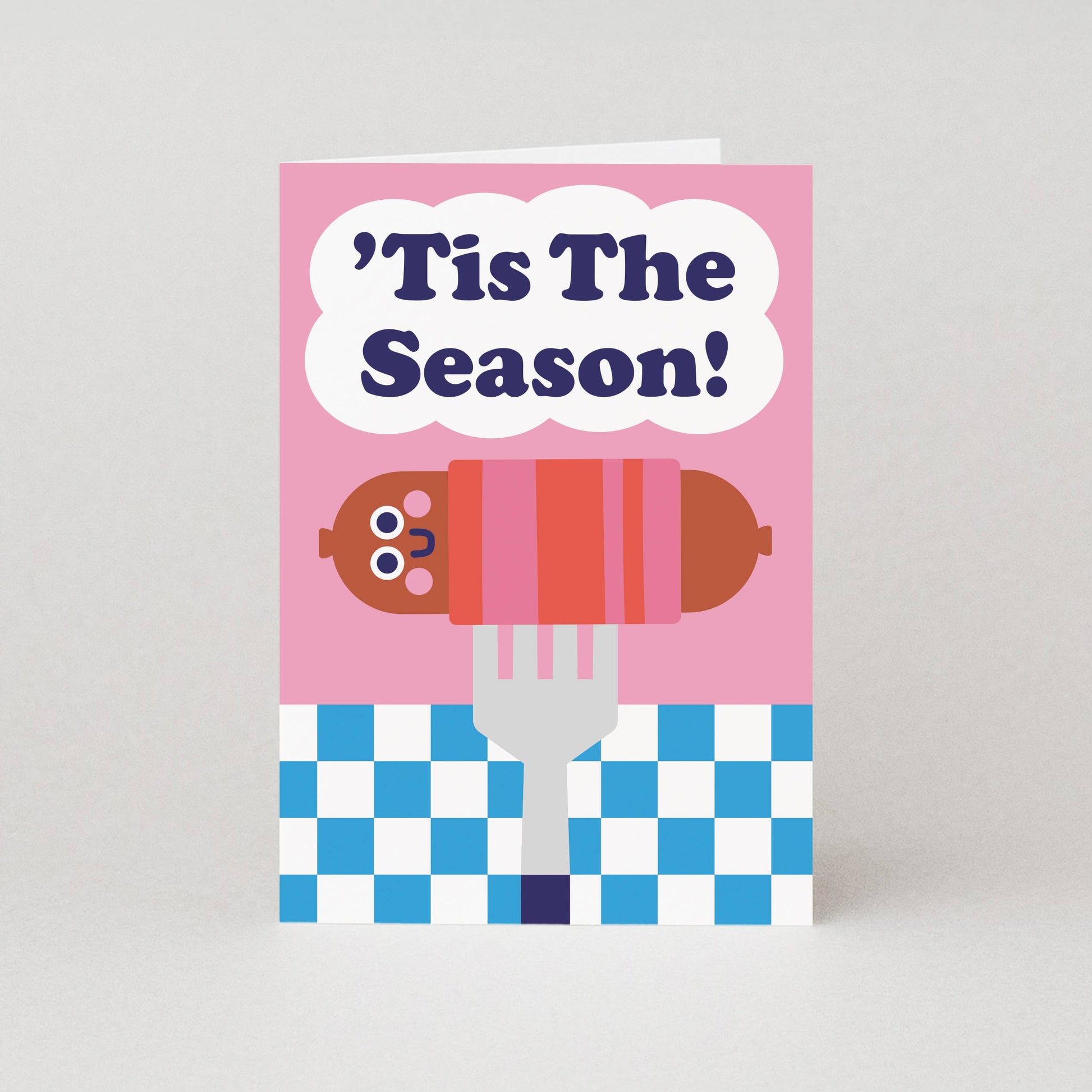 Card with a cartoon hot dog on a fork and 'Tis The Season text on a pink background