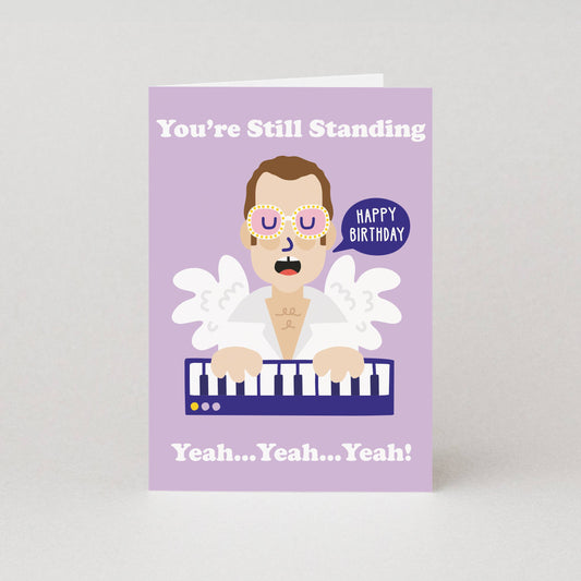 Birthday card with a cartoon character Elton Johnplaying keyboard and text on a purple background