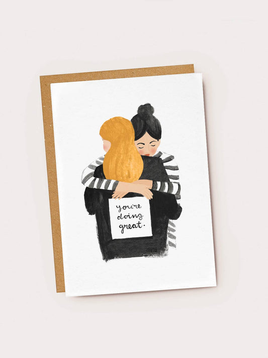 Card with illustration of two people hugging, one holding a sign saying 'You're doing great.' on a white background.